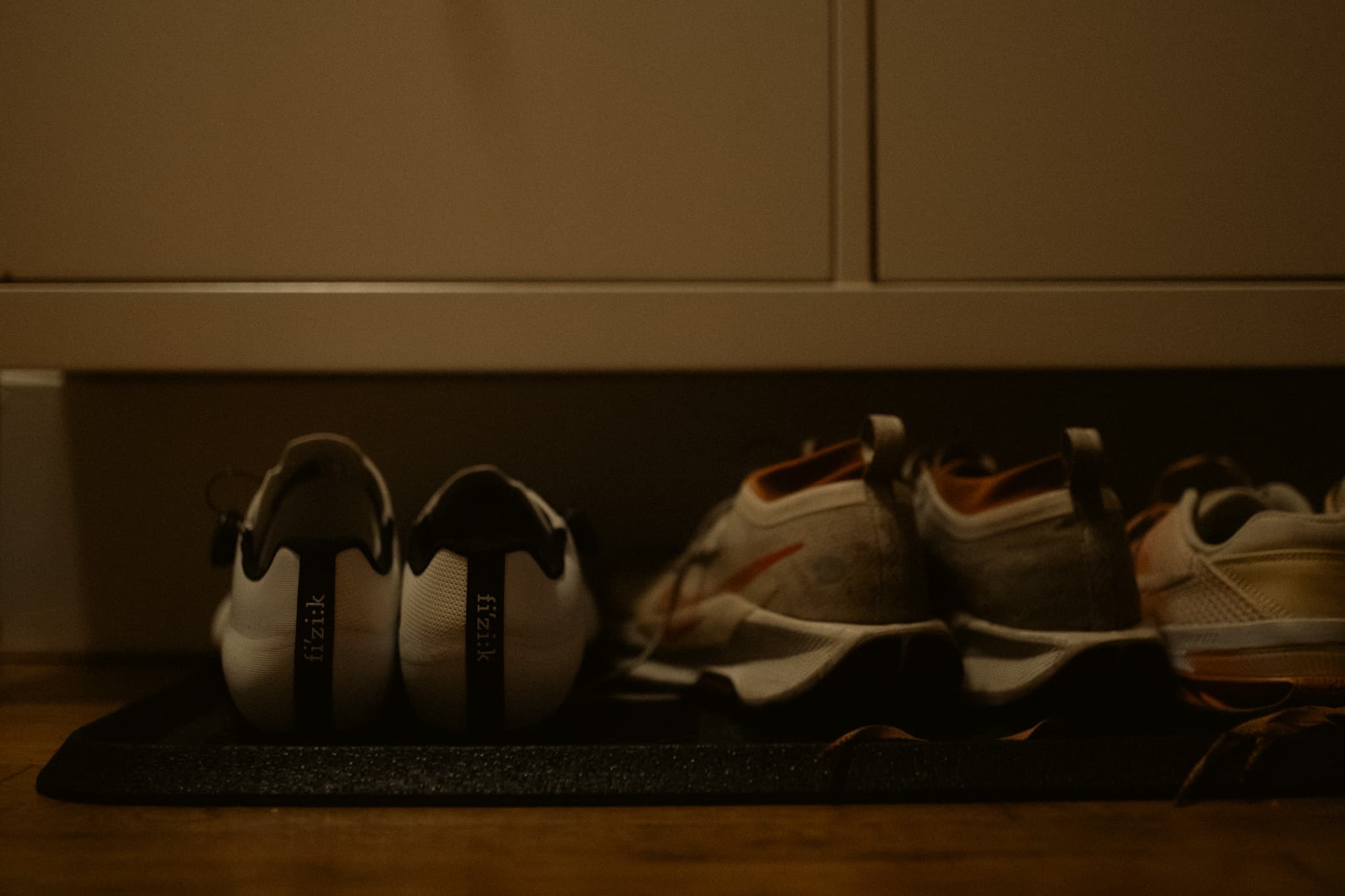 Cycling shoes and sneakers lined up on a mat by the door